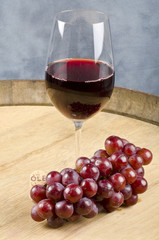 Glass of Red Wine and Bunch of Grapes on a Barrel
