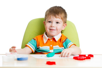 Happy little kid sitting at table and playing with colorful clay