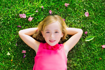 Blond kid girl lying on garden grass smiling aerial view