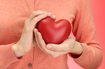 Red heart in woman hands, on red background