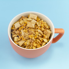 Orange Mug full of cereals on light blue background.