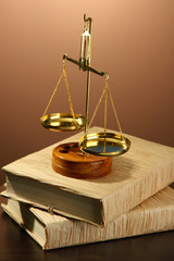 Gold scales of justice and books on brown background