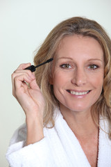 Blond woman in bathrobe holding mascara brush
