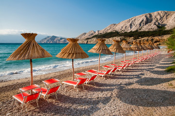 Sunshades and orange deck chairs on beach at Baska - Krk - Croat