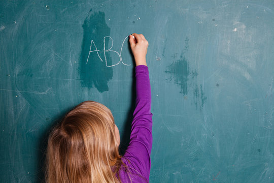 Young girl writing letters on chalkboard