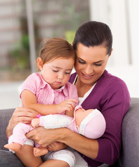 happy mom playing doll with little daughter on sofa