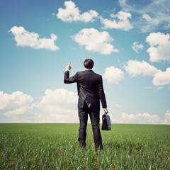 businessman standing in the field and points a finger at somethi