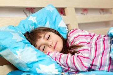 beautiful little girl sleep in bed under a blue blanket
