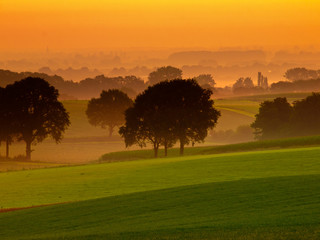 Orange sunrise over misty and hilly farmland