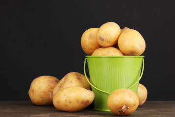 Ripe potatoes in pail on wooden table on black background