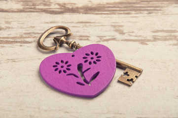 violet wooden heart on wooden desk with key and ribbon