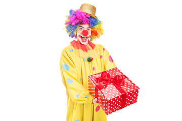 A happy male clown holding a red present