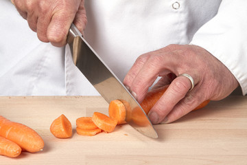 Chefs hands chopping carrot on wooden board