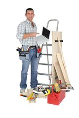 Carpenter stood by ladder with laptop