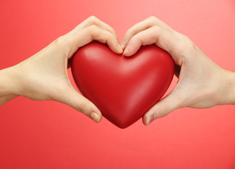 Red heart in woman and man hands, on red background