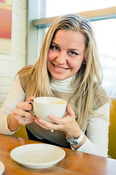 smiling young woman drinking coffee from a white cup