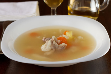 soup with fish in white plate with glass of wine