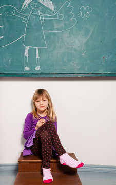 Young girl sitting in front of chalkboard