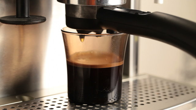 Coffee drips into a dark glass in espresso coffee machine