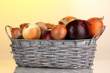 Ripe onions in grey basket on yellow background