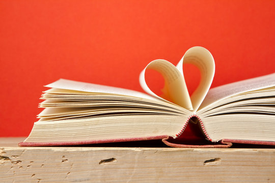 Book with pages folded in heart shape over red background