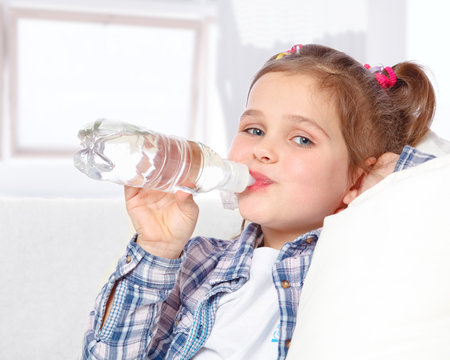 portrait of a cheerful little girl drinking water from a bottle