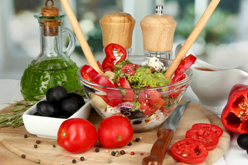 Fresh greek salad in glass bowl surrounded by ingredients for