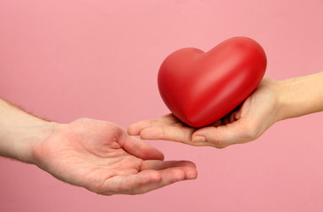 Fototapeta na wymiar Czerwone serce na dłoni kobiety i mężczyzny, na różowym tle