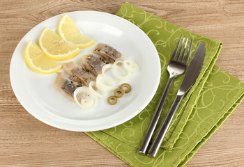 Dish of herring and lemon on plate on wooden table close-up