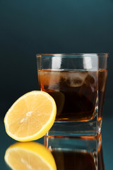 Glass of whiskey with ice and lemon on blue background