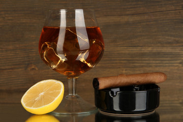 Glass of brandy with ice and lemon on wooden background