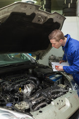 Mechanic with clipboard examining car engine