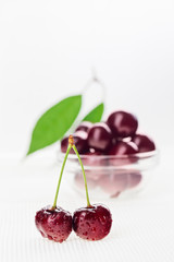 Still life with pair of red wet cherry fruit and glass bowl, on
