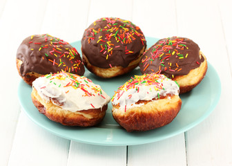 Tasty donuts on color plate on light wooden background