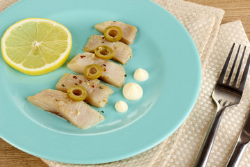 Dish of herring and lemon on plate on wooden table close-up