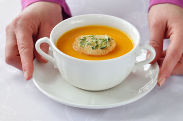Serving homemade roasted pumpkin soup in white bowl on white tablecloth.