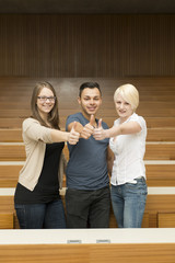 Zwei Studentinnen und ein Student zeiten ihren Daumen nach oben
