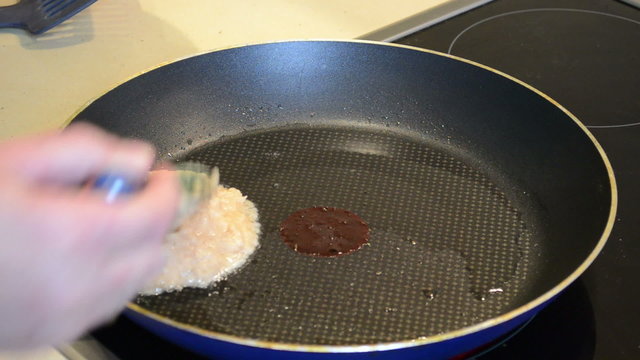 hand with spoon put shreddered potatoes into pan baking pancakes