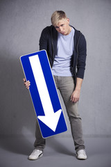 Miserable man holding direction arrow sign pointing down. - obrazy, fototapety, plakaty