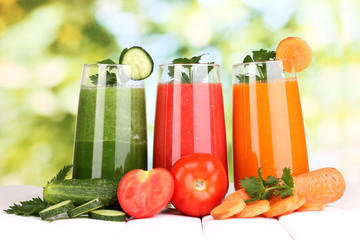 Fresh vegetable juices on wooden table, on green background