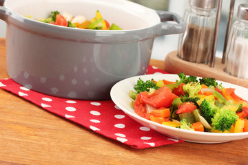 Vegetable stew in gray pot on wooden table on bright background