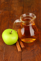 Full jug of apple juice and apple on wooden background
