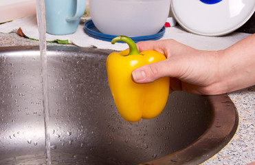 woman washes peppers under water in the kitchen