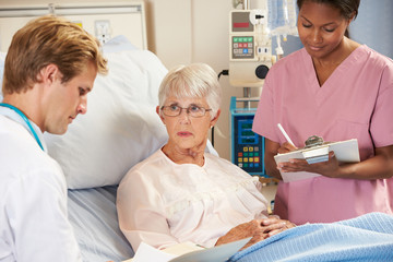 Fototapeta premium Doctor With Nurse Talking To Senior Female Patient In Bed