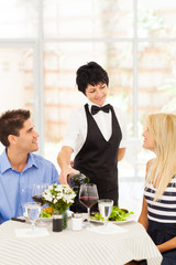 friendly mature waitress serving wine to diners in restaurant