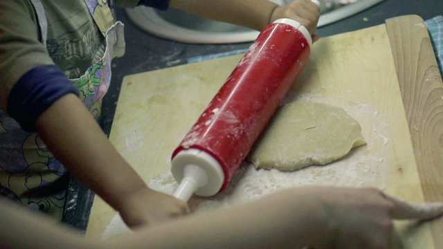 Small children hands with dough on wooden table with flour, slow