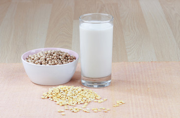 A glass of soy milk with a bowl of raw soybean and soybean seed