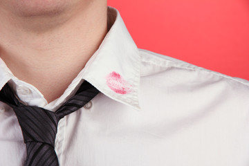 Lipstick kiss on shirt collar of man, on red background