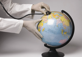 Close-up of human hands examining a globe with a stethoscope