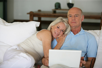 Fototapeta premium Middle-aged couple in bed with laptop